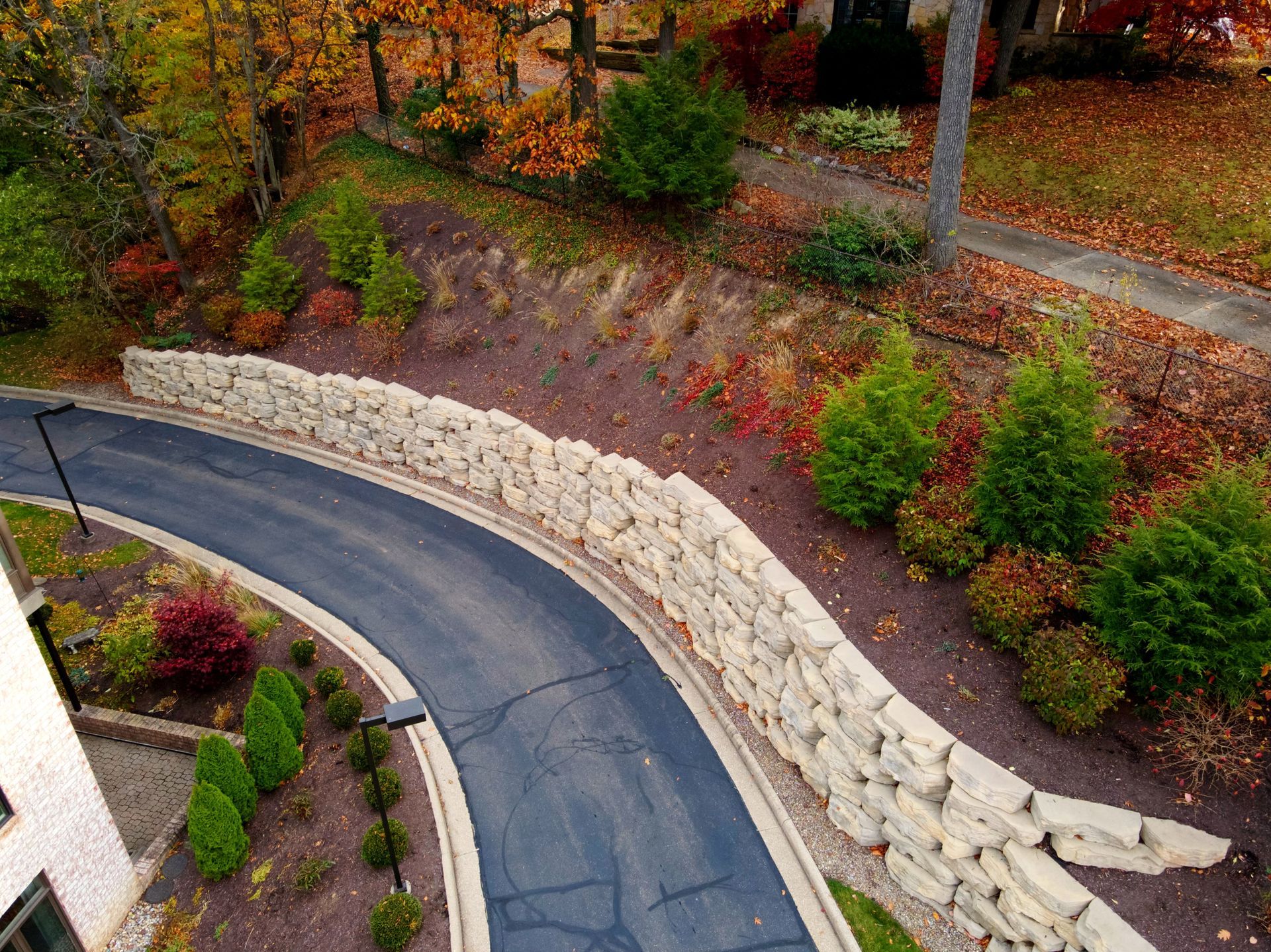 Curving road bordered by a stone retaining wall and lush landscaping in an autumn setting.