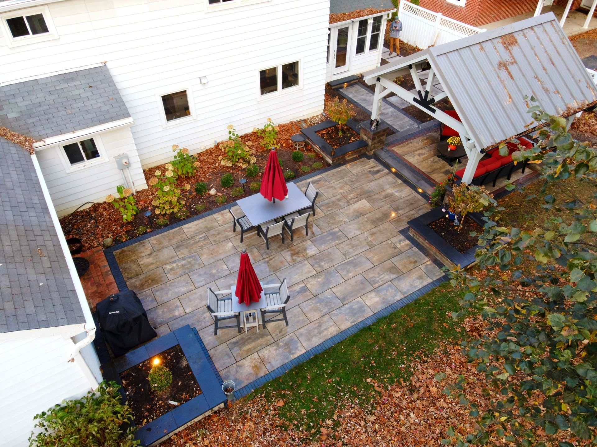 Aerial view of a backyard patio with dining sets, umbrellas, and a pergola.
