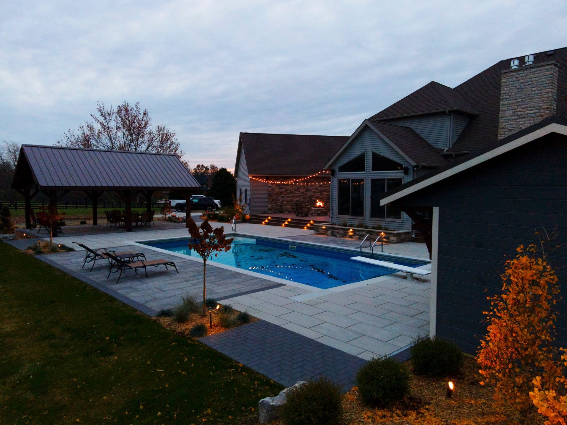 Backyard pool with a house, gazebo, and lights at dusk.