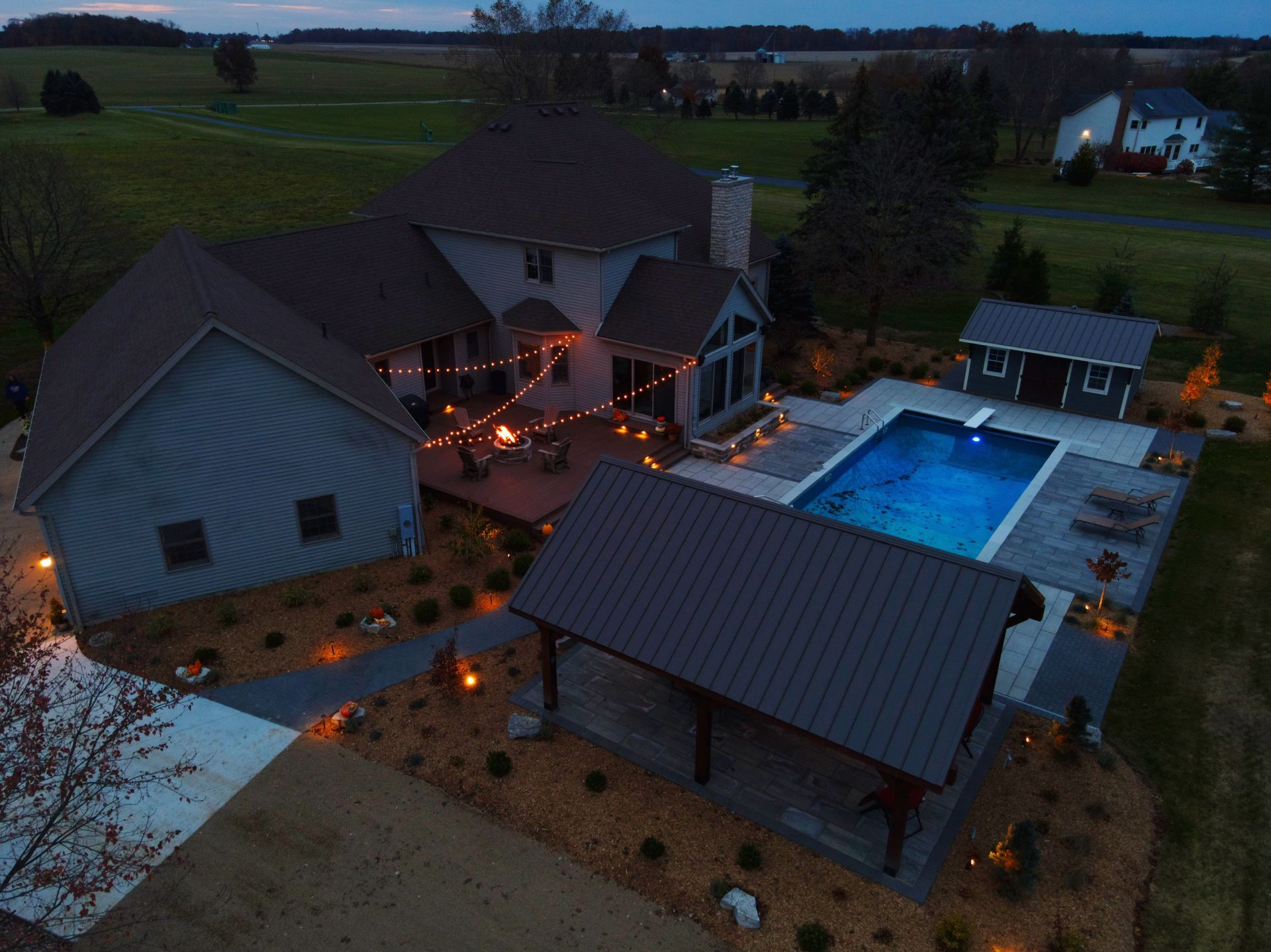Aerial view of a home with an illuminated pool and patio area, set against a twilight sky.