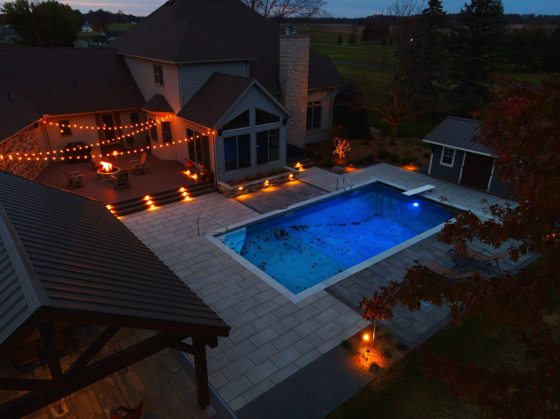 Paver patio with pool, landscaping, and outdoor lighting at dusk.