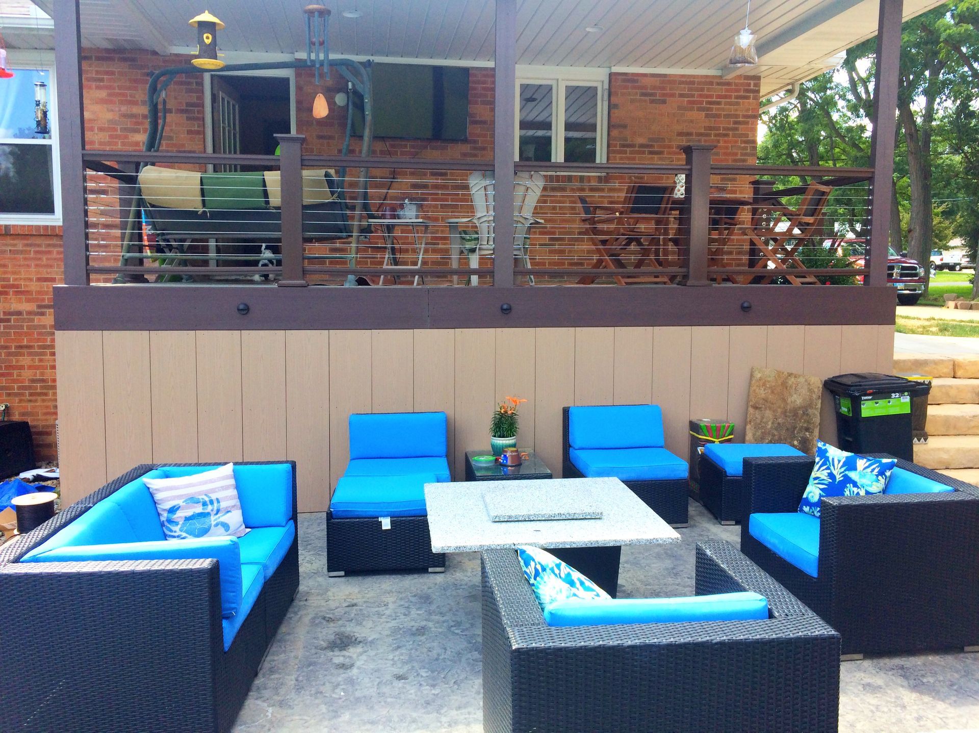 Patio with black wicker furniture, blue cushions, fire pit, and brick house.