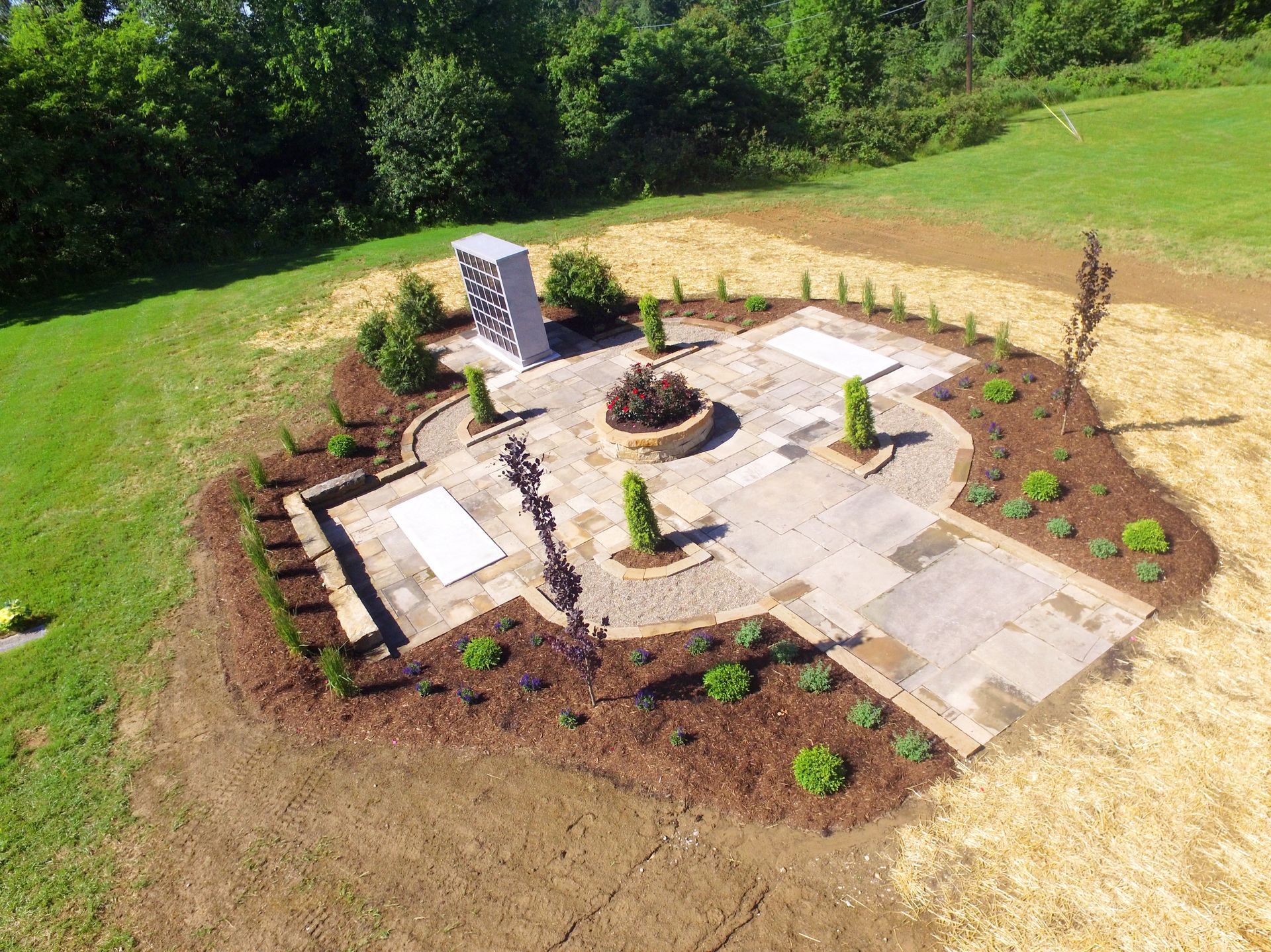 Aerial view of a landscaped outdoor memorial. Stone pathway with memorial pillar and various plantings.