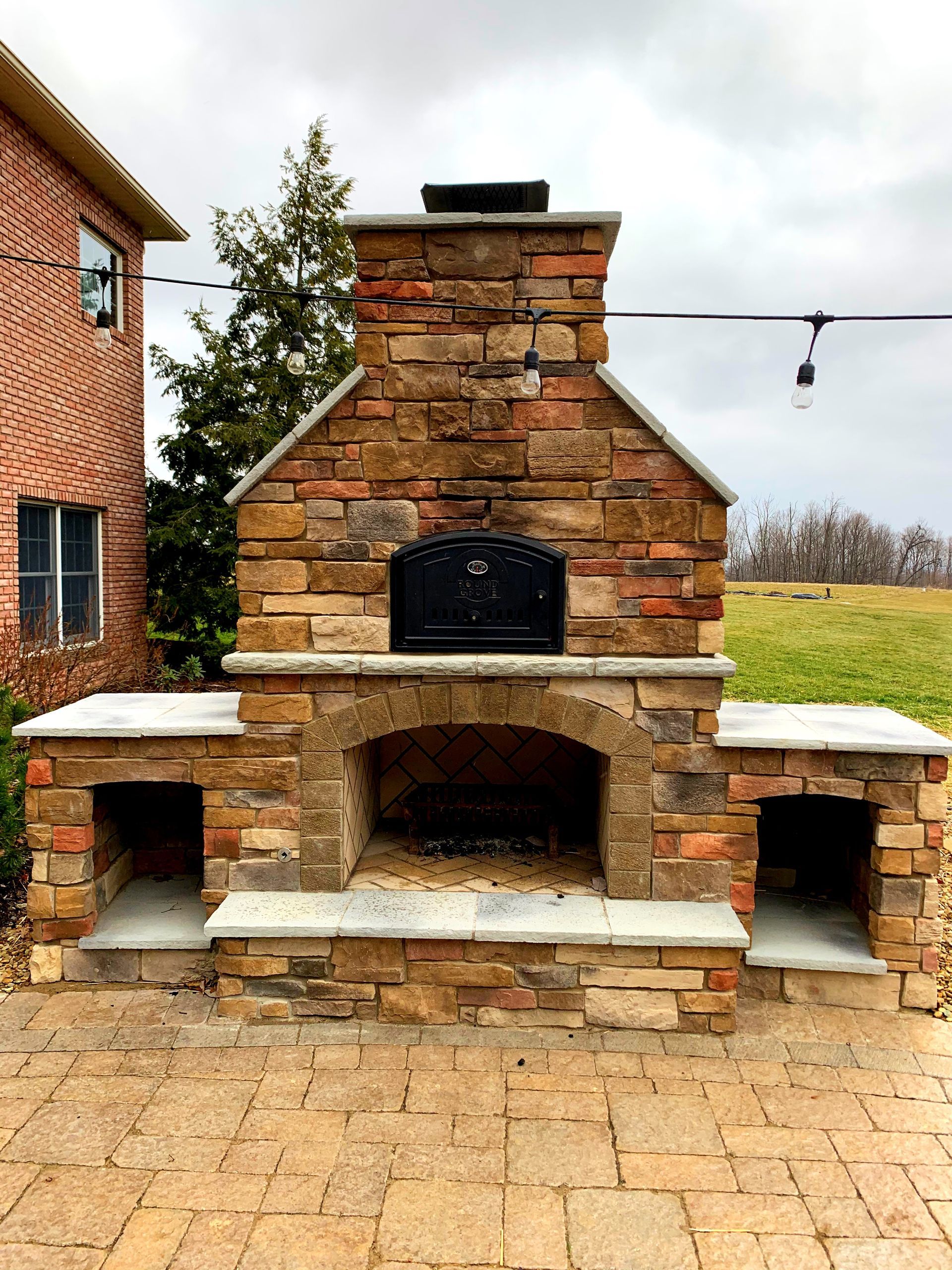 Outdoor brick pizza oven with a black door, flanked by storage compartments, on a stone patio.