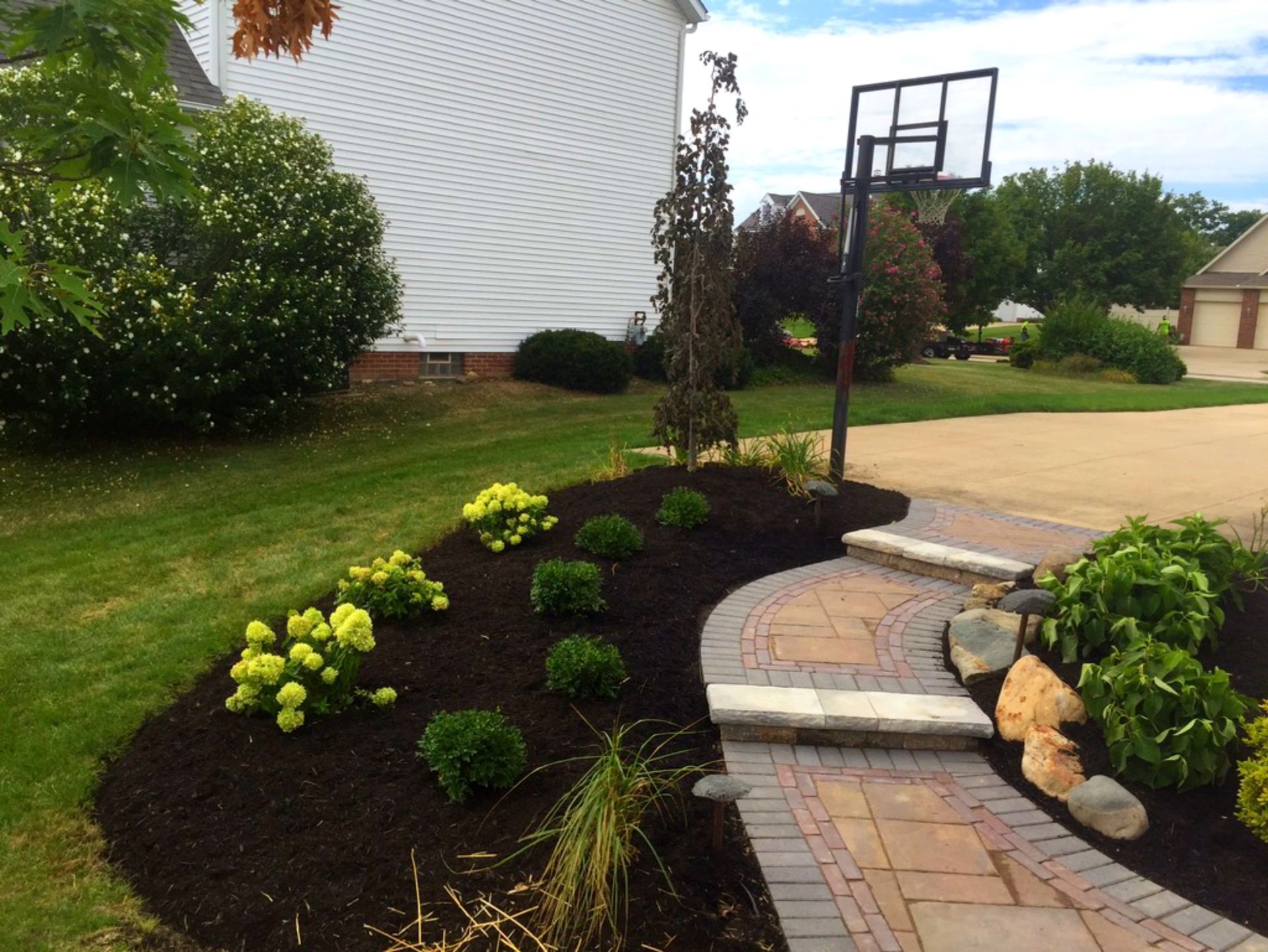 Curved brick pathway with landscaped bed and basketball hoop in front yard.