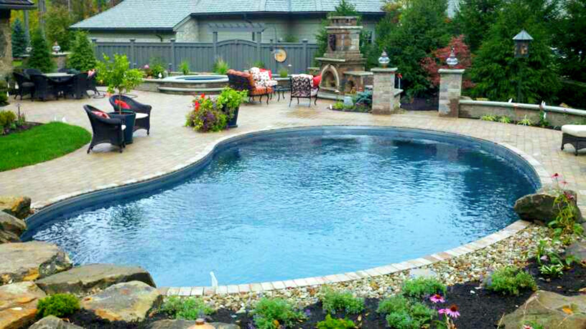 Exterior of a modern house with paver patio, pool, and manicured landscaping, illuminated at dusk.