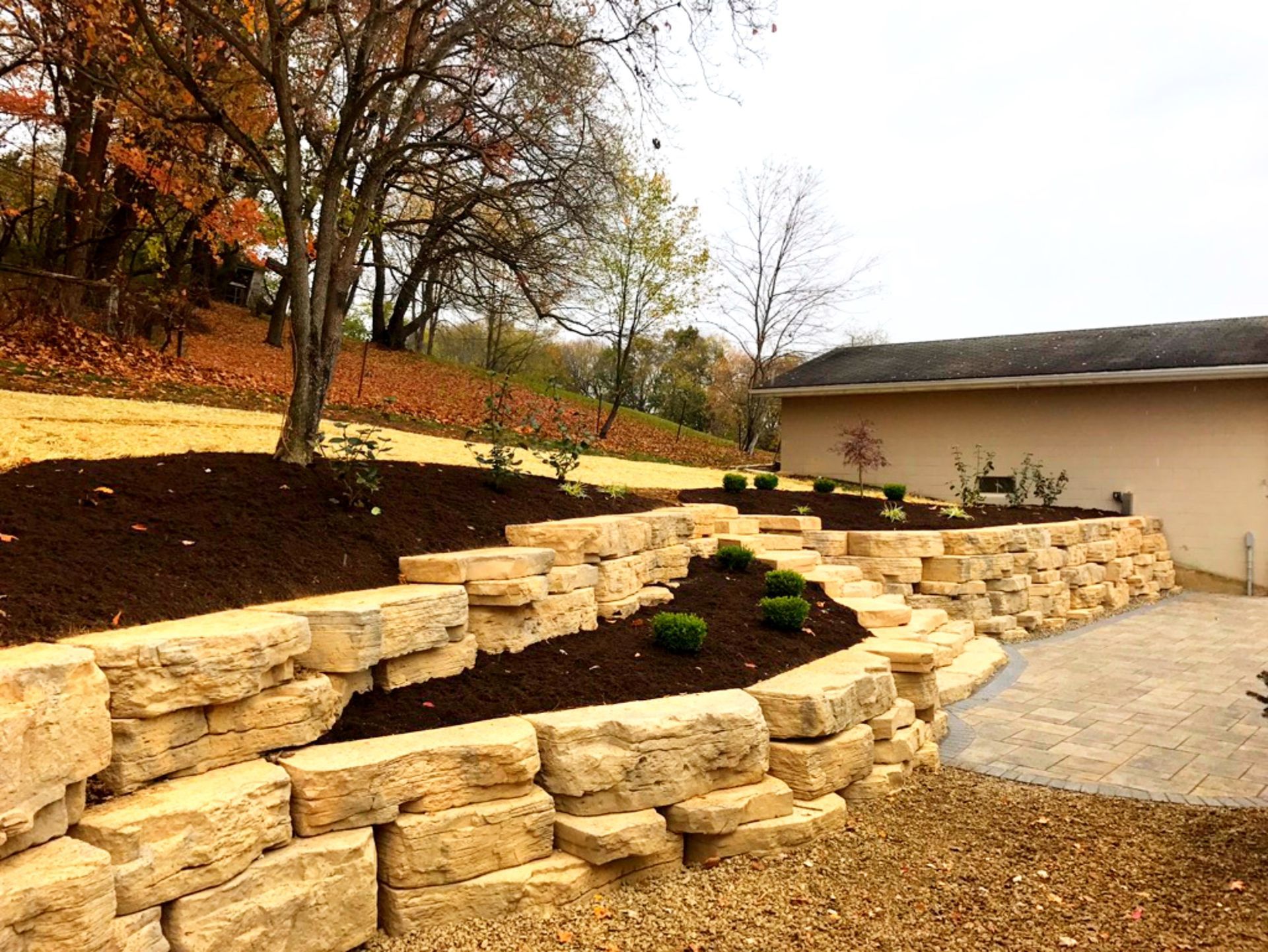 Stone retaining wall with tiered garden beds, brown mulch, and small green shrubs.