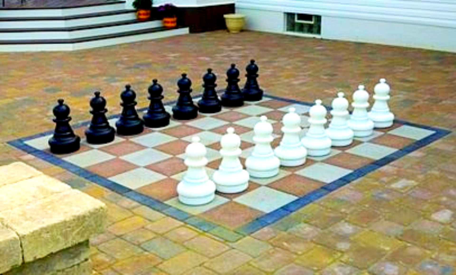 Giant chess set with black and white pieces on a checkerboard patio.