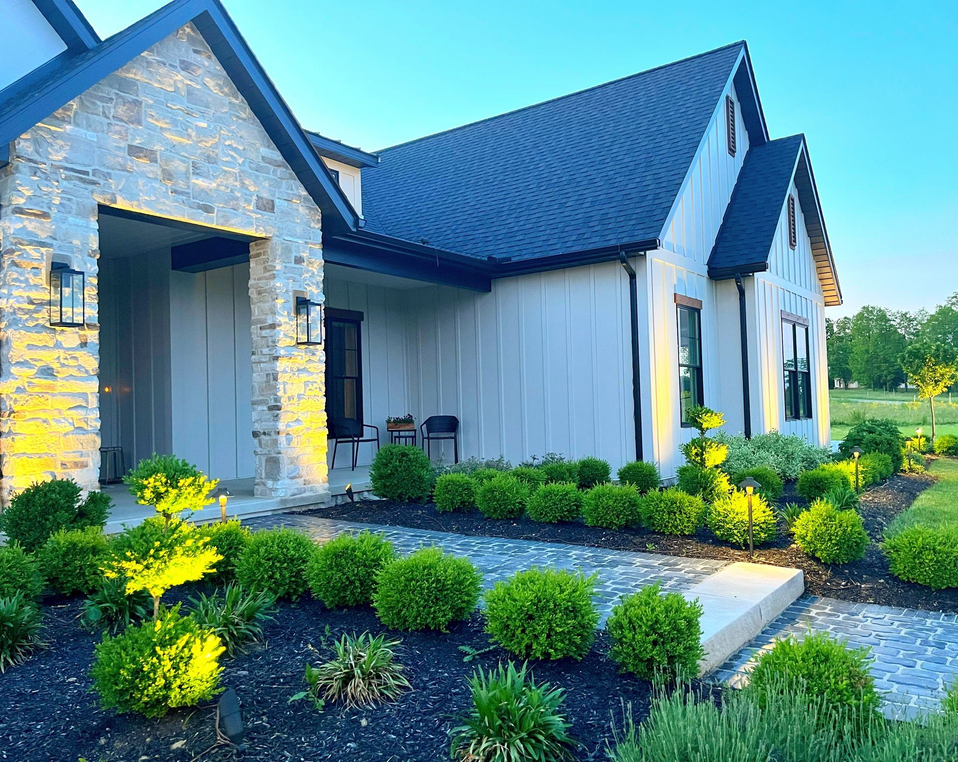 A modern white house with black roof and trim. Landscaping with illuminated shrubs and stone walkway.
