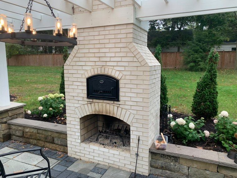 Brick outdoor fireplace with black metal oven door, patio, and backyard.