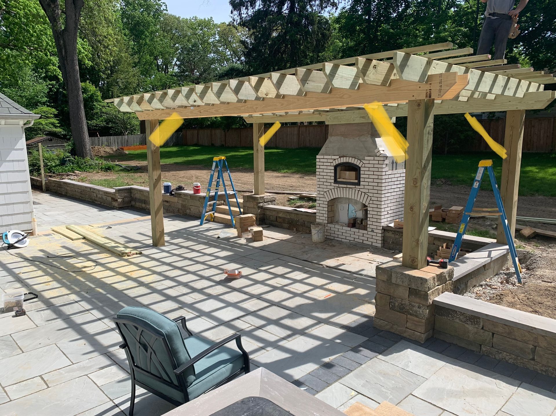 Pergola construction over a patio with a brick oven and retaining wall.