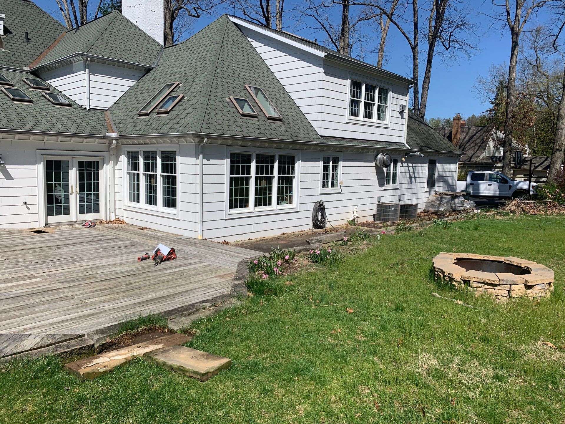 White house with green roof, deck, and fire pit in yard.