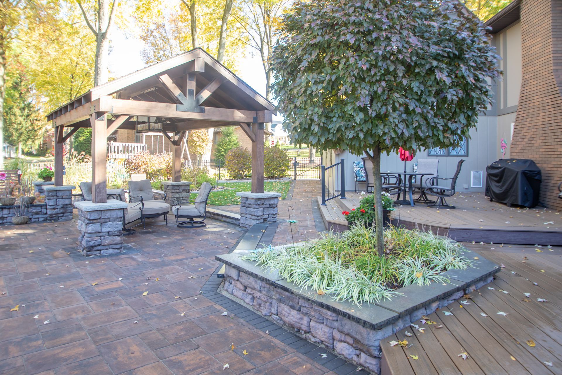 Patio with pergola, seating area, and tree in a raised bed, near a house with deck.