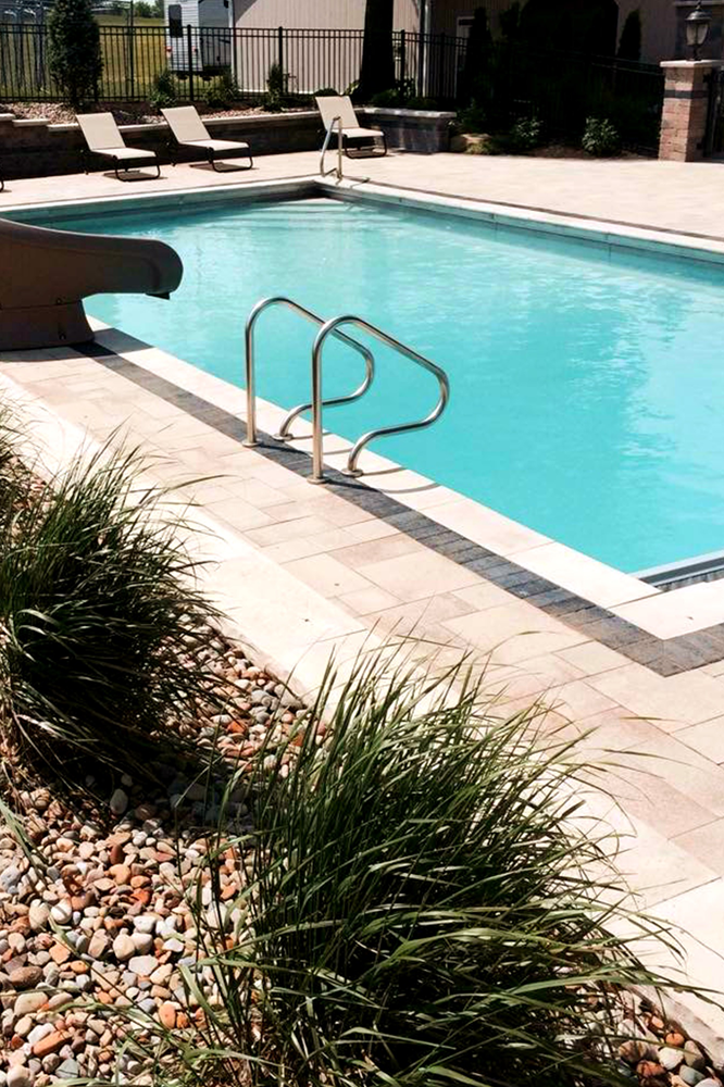 Swimming pool with chrome ladder, slide, and deck. Landscaping with shrubs and stones.