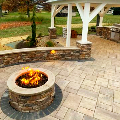 Stone patio with a fire pit, gazebo, and built-in grill in a yard.