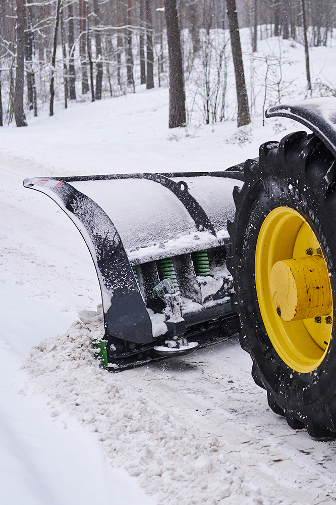 A tractor with snow plow clearing a snowy road. Green and yellow details.