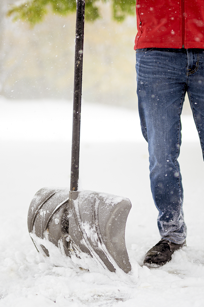 Person shoveling snow with a large shovel; snowing outdoors.