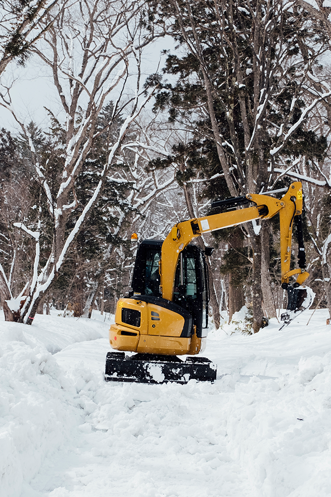 Yellow excavator clearing a snowy path in a forest.
