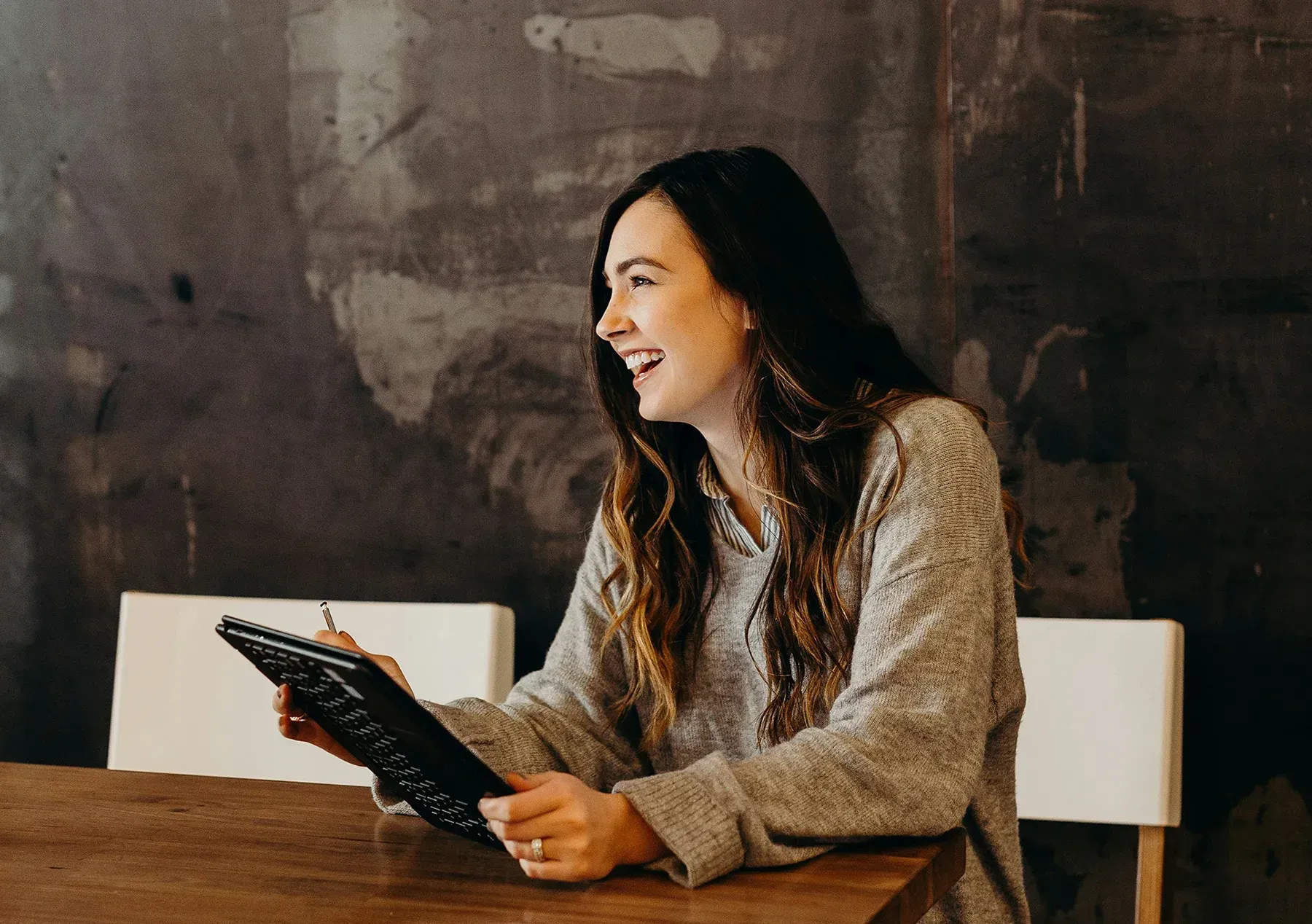 Woman smiling at a table, holding a tablet in a rustic café-like setting
