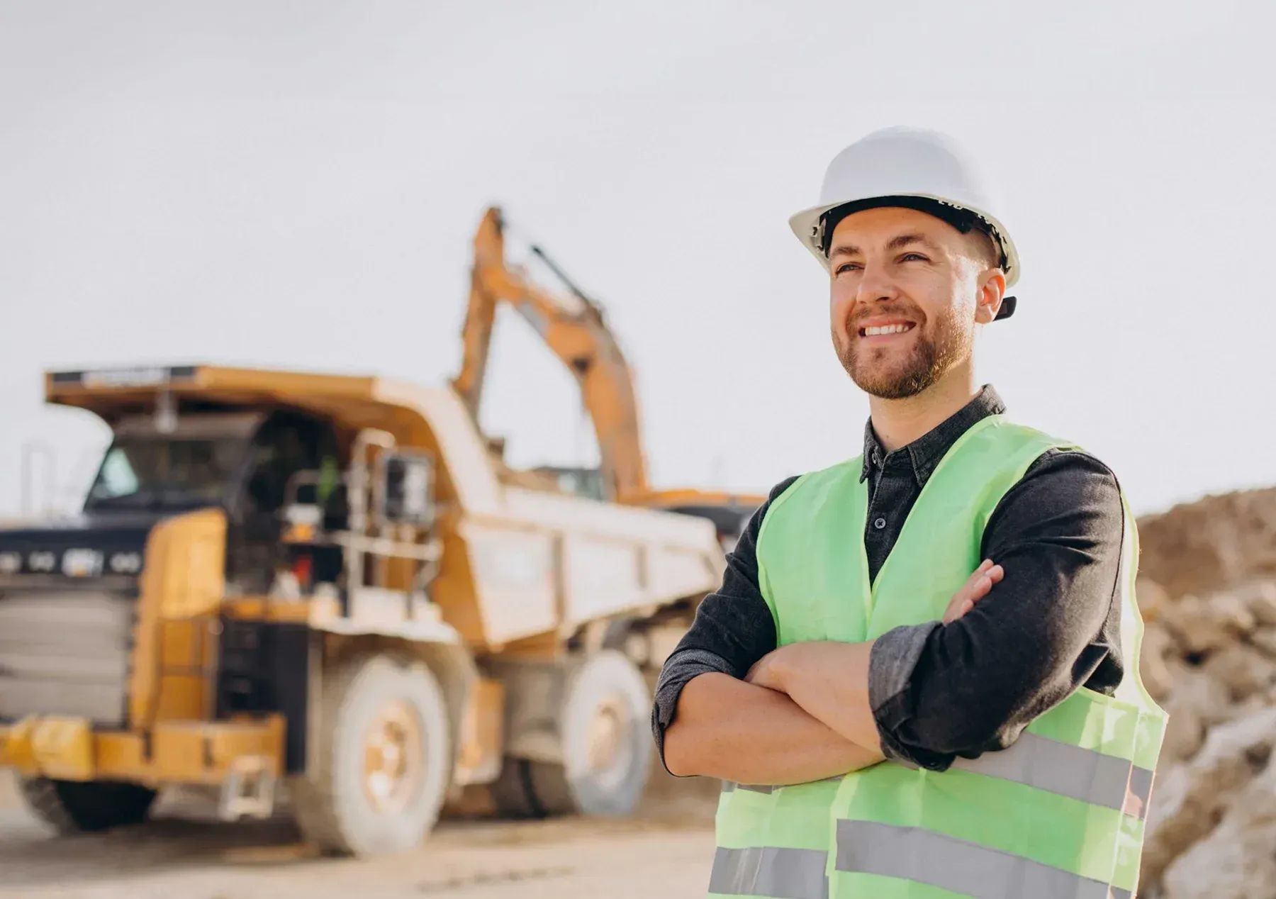 Construction worker in a hard hat and safety vest standing before heavy machinery on a job site