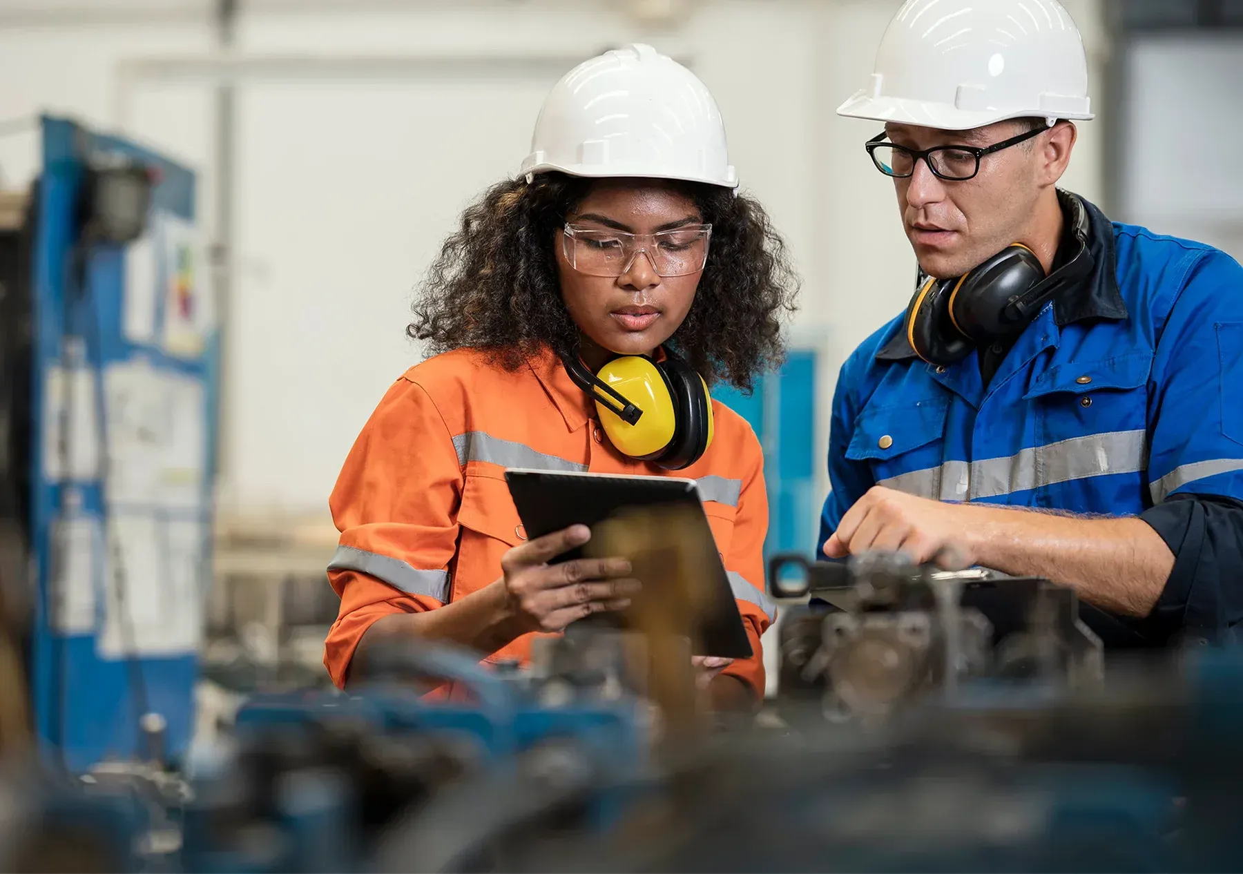 Two workers in hard hats reviewing a tablet in an industrial workshop