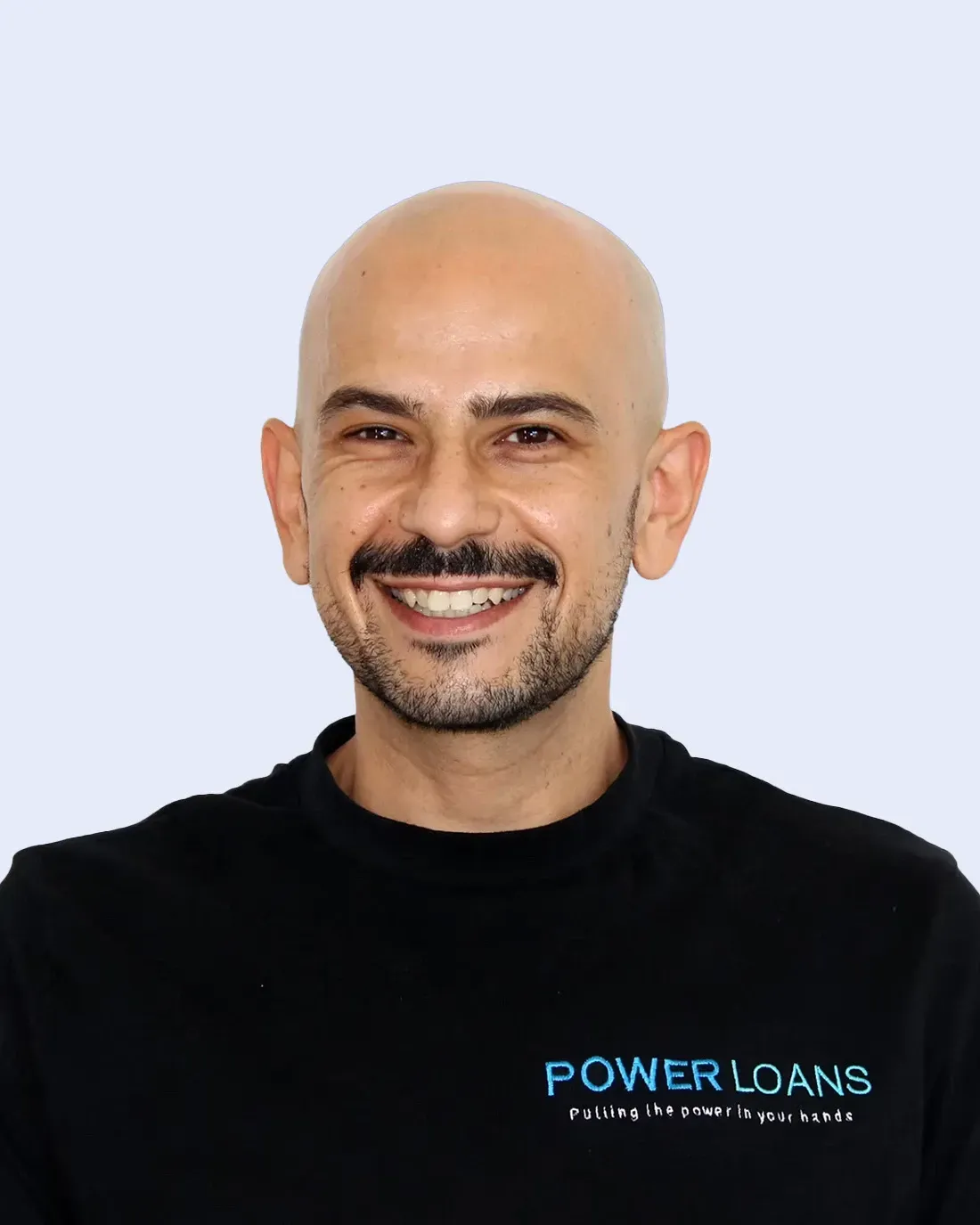 Smiling bald man in black Power Loans shirt against a light blue background