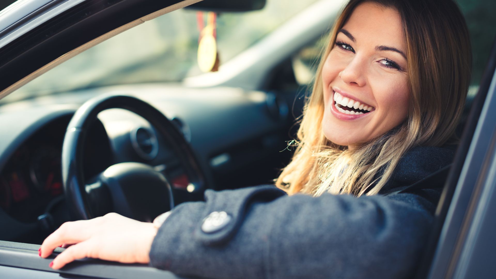 Smiling person sitting in the driver’s seat of a car, leaning out the open window