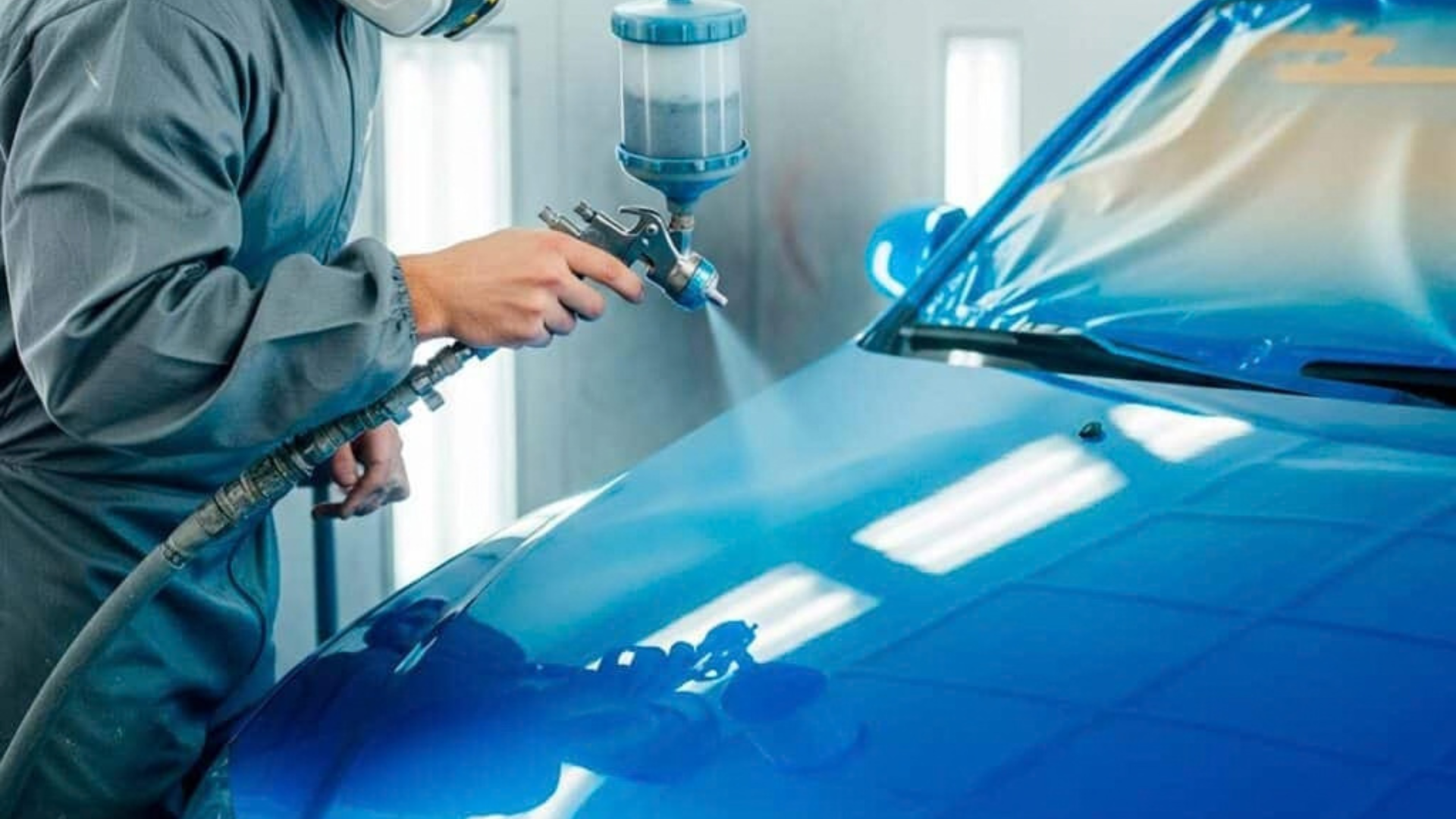 Worker spray-painting a blue car in a auto body shop