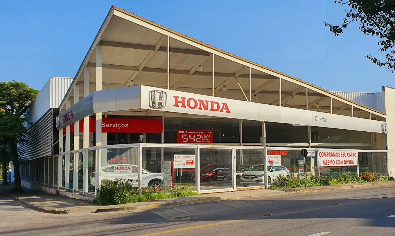 Fachada de concessionária Honda com sinalização vermelha e janelas de vidro sob um telhado triangular.
