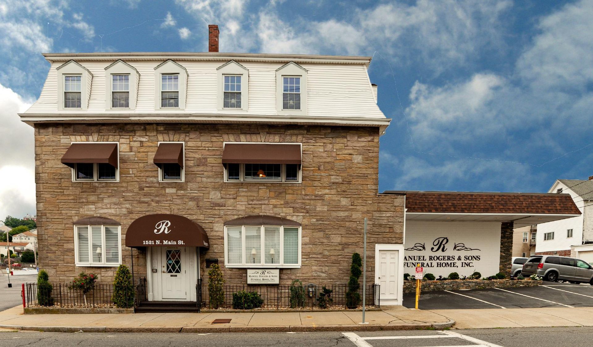 Stone building with white roof and awning, and a garage beside it under a blue sky.