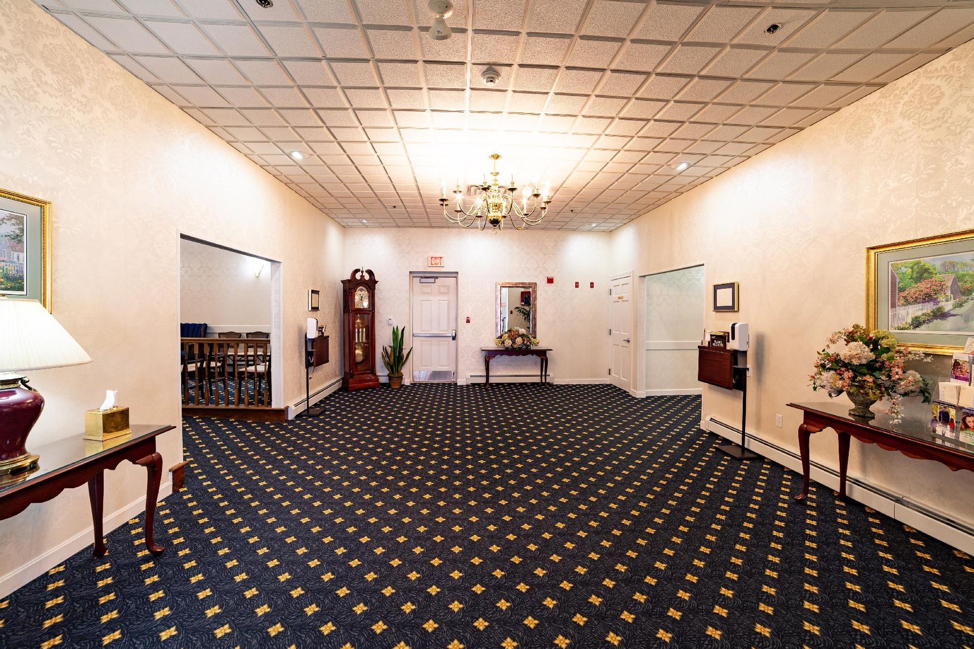 Empty hotel lobby with patterned carpet, cream walls, chandeliers, and tables with floral arrangements