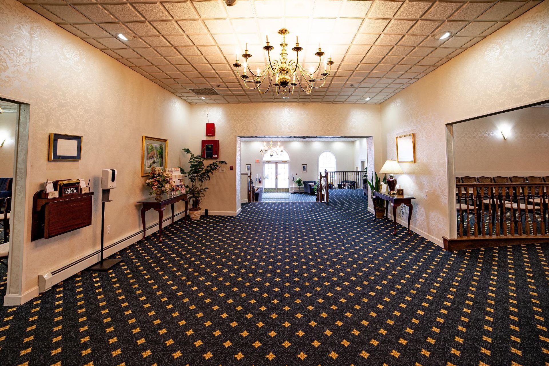Empty hotel lobby with patterned carpet, chandeliers, and chairs lining the walls