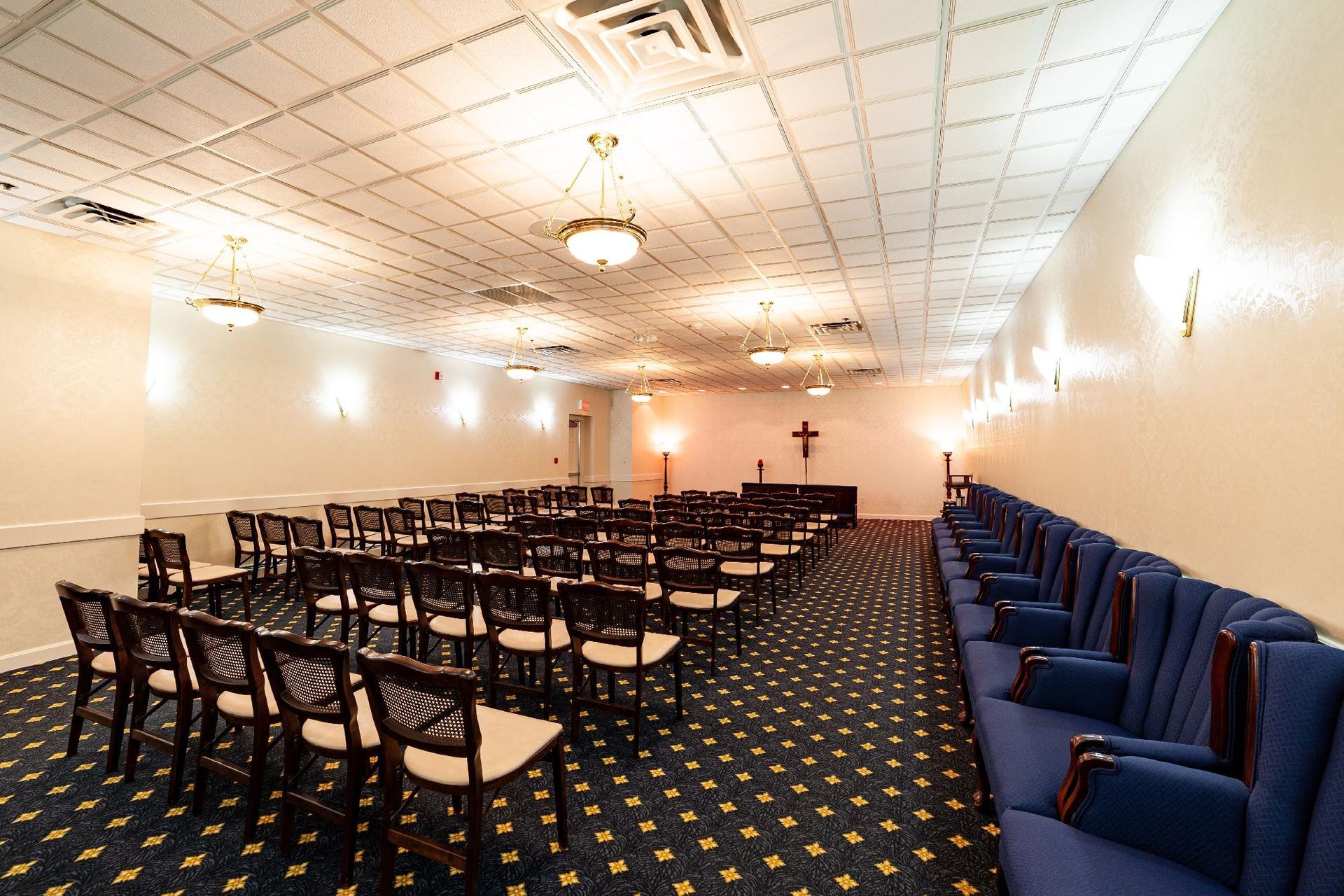Small conference room with rows of chairs, a long table, blue couch seating, and a cross at the front.