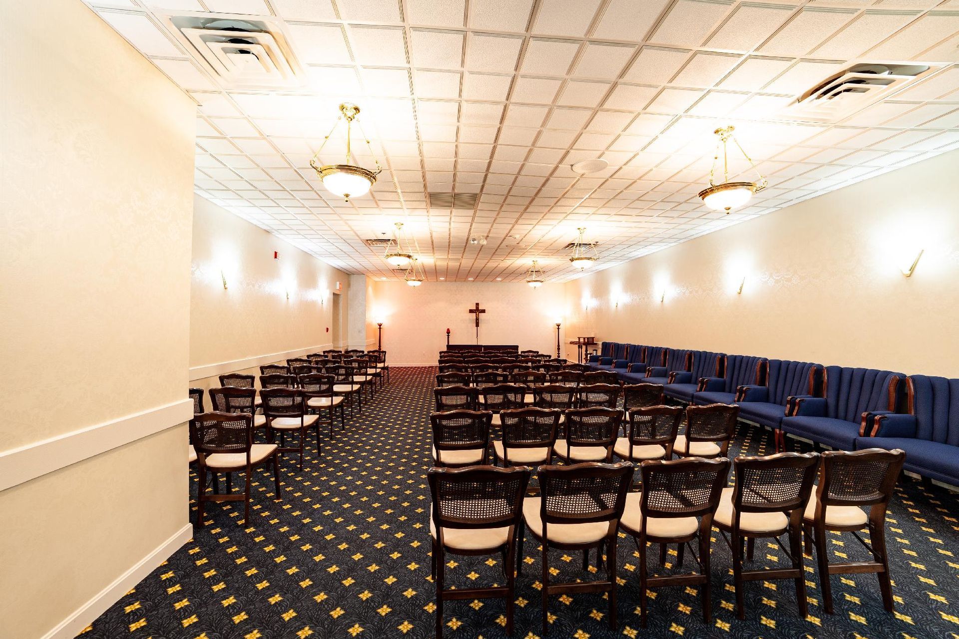 Empty banquet hall with rows of chairs, blue wall seating, and patterned carpet under ceiling lights