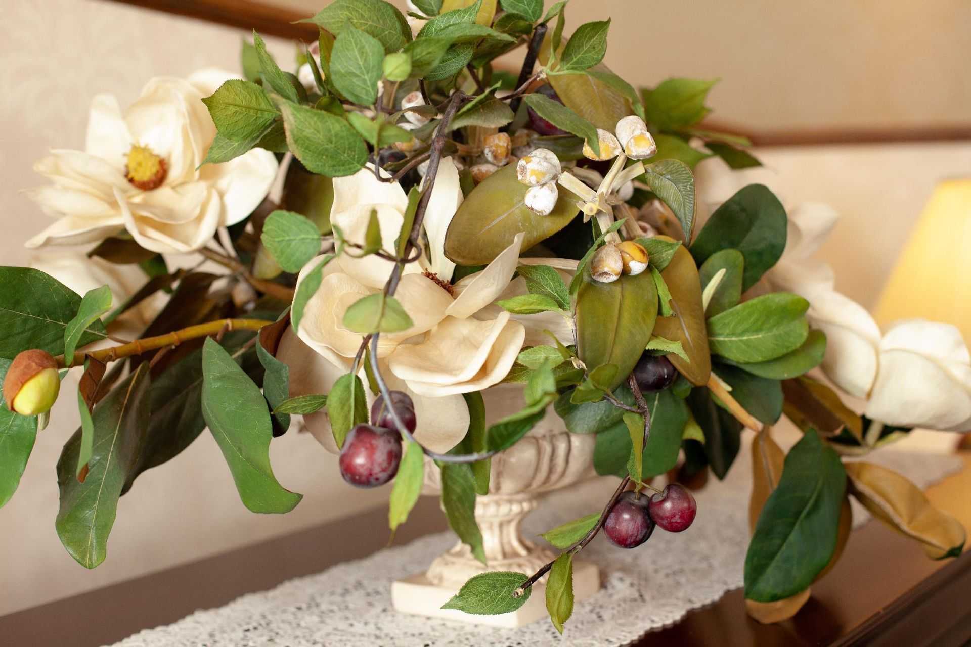 White and pink floral arrangement with green leaves and purple berries in a decorative vase