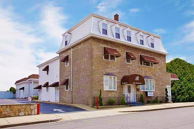 Brick building with white dormer windows and awnings on a sunny street corner