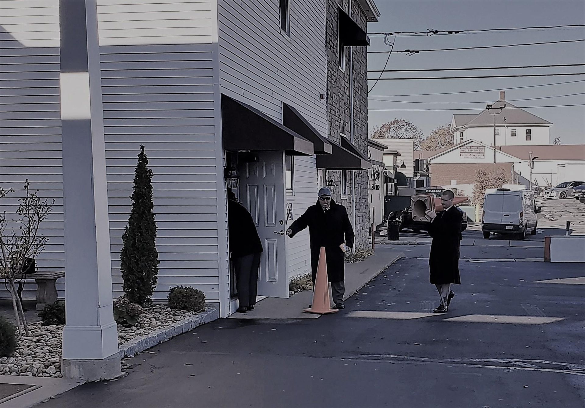 Two people walking outside a building, one carrying a long wooden board on a quiet street.