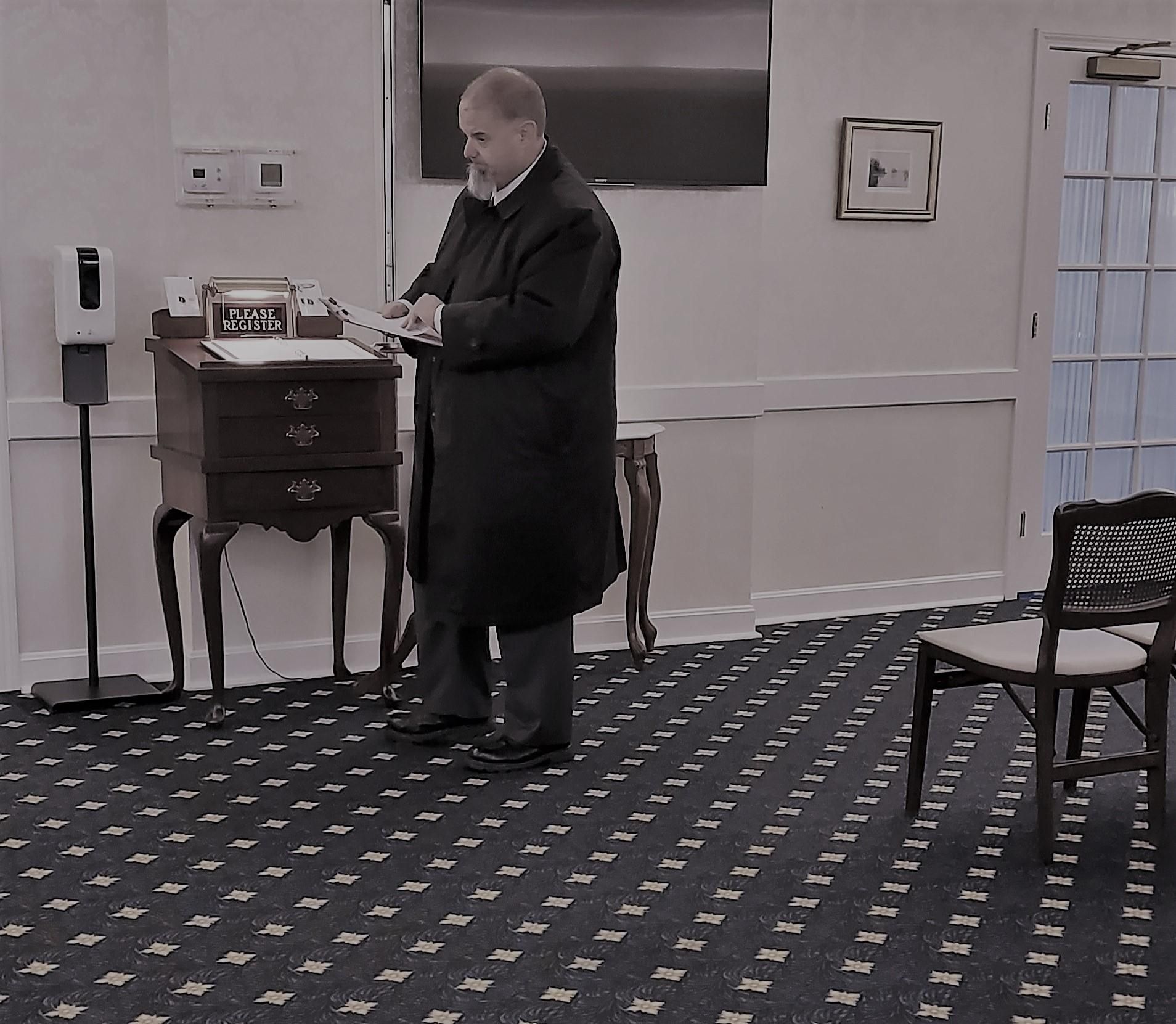 Man standing by a small wooden table in a carpeted hallway, looking at something in his hands.