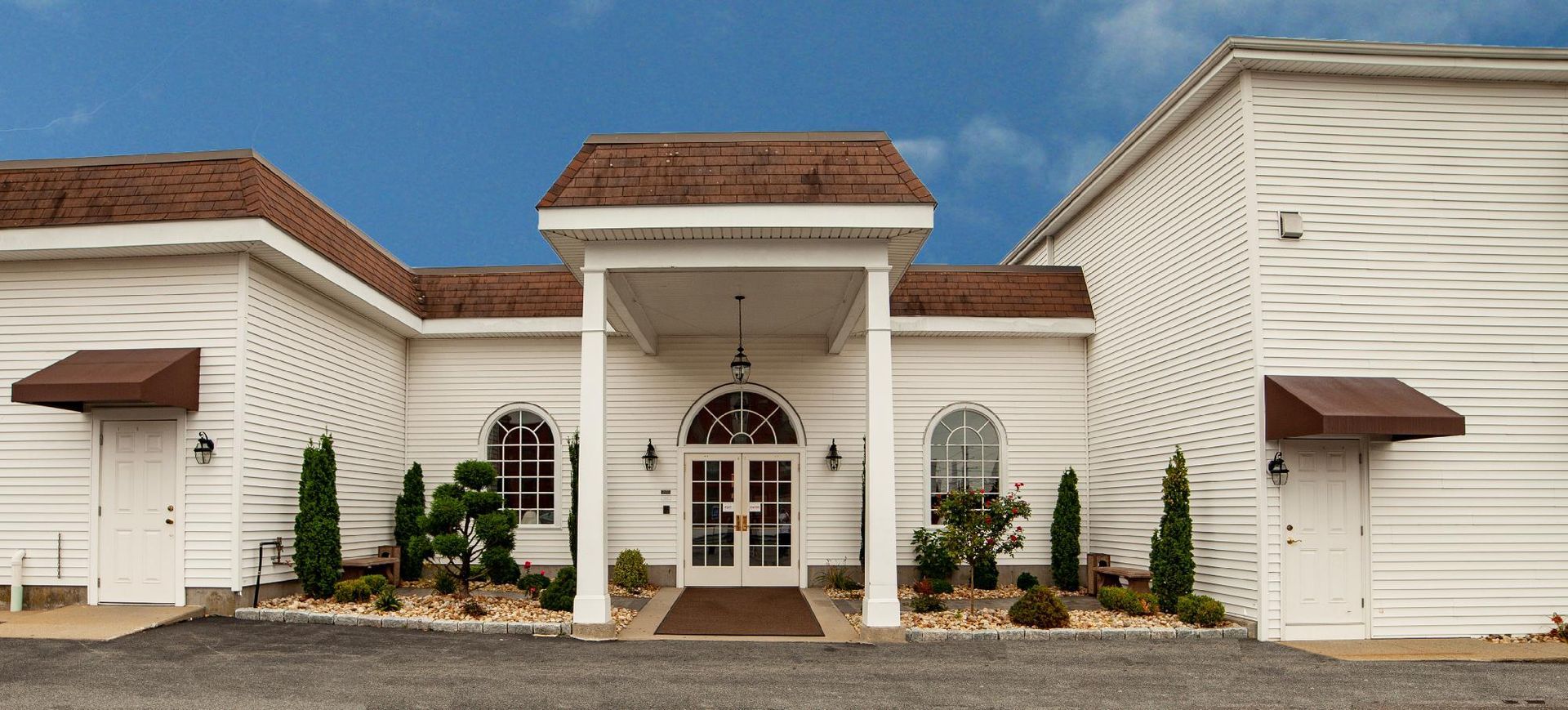 White stucco house with arched front entrance, brown roof, and small landscaped entryway