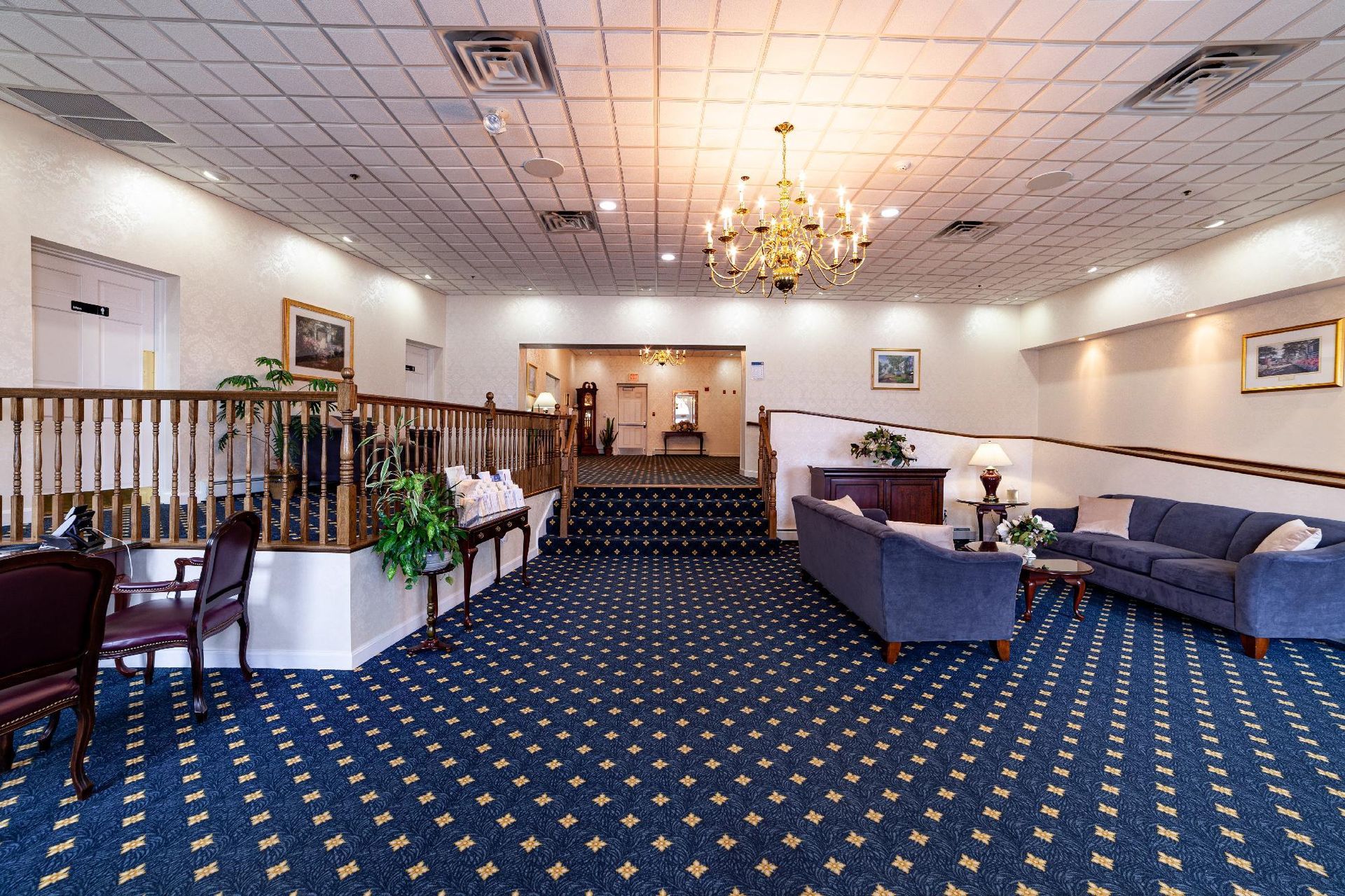 Hotel lobby with blue carpet, seating area, chandelier, and reception desk