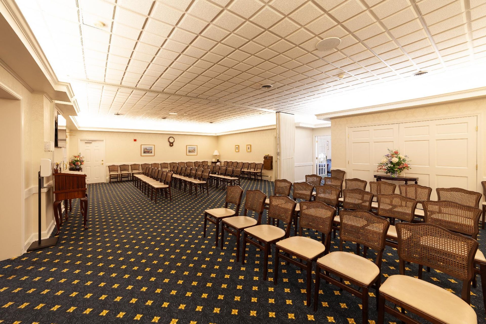 Empty banquet hall with rows of chairs, patterned carpet, and a bright coffered ceiling