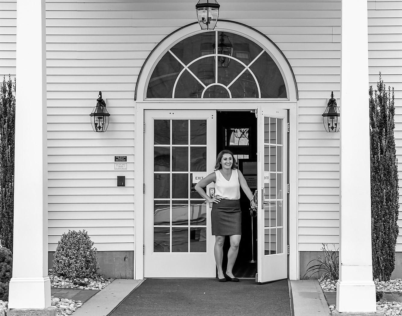 Woman standing in a doorway of a white house with arched glass window and columns