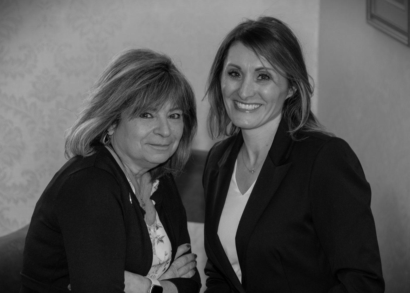 Two women in dark blazers smiling and posing indoors