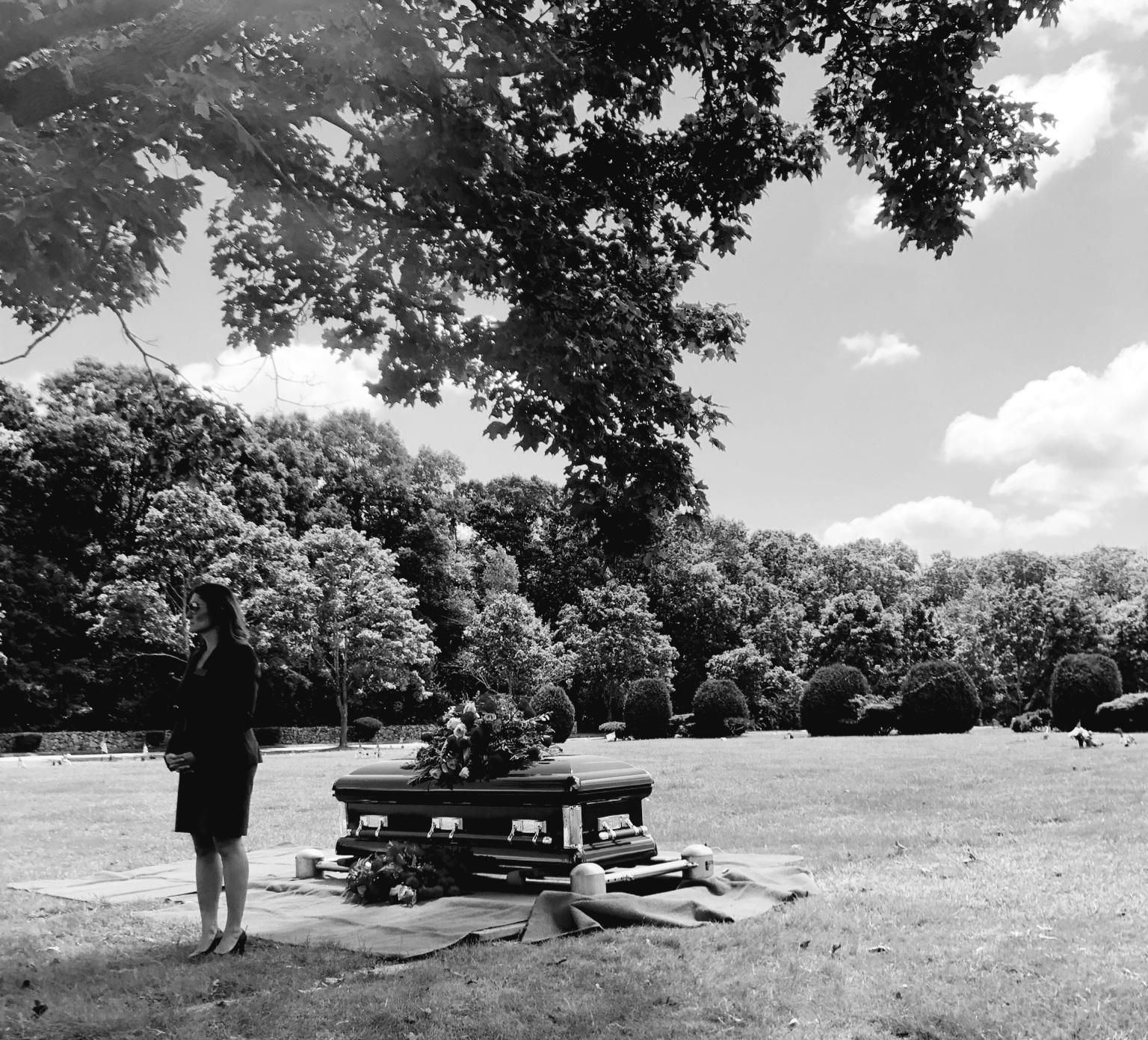 A person stands by a picnic table under a large tree in a sunny park.