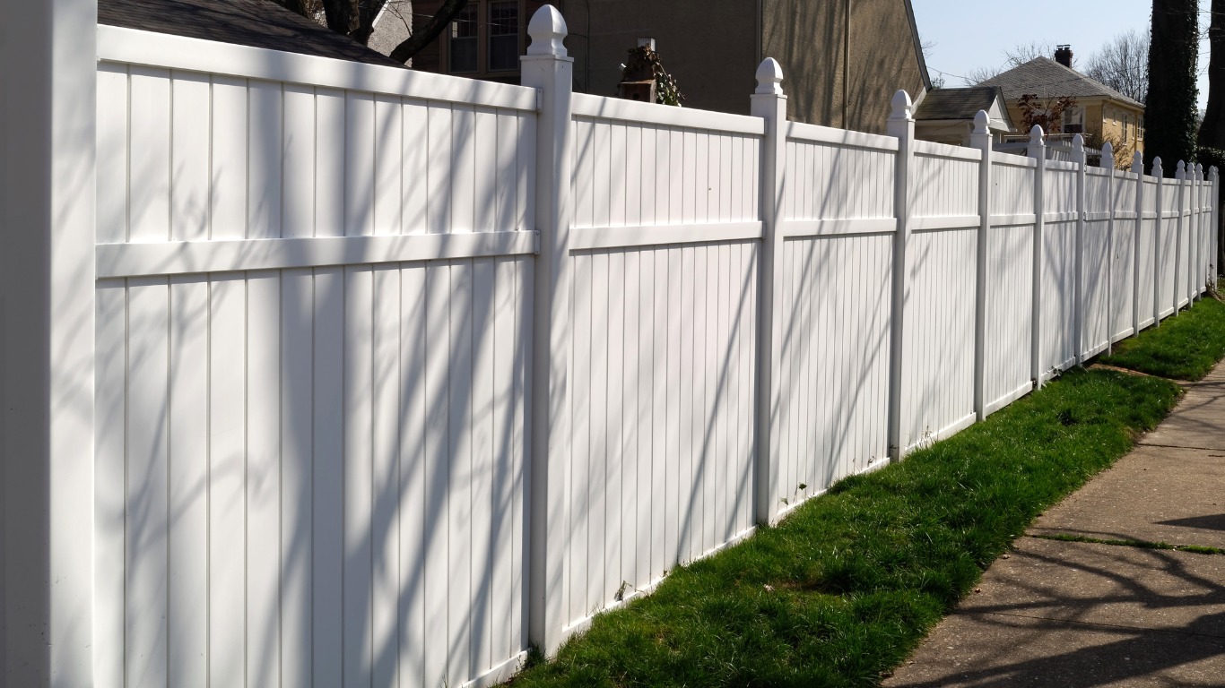 A white fence along a sidewalk next to a house.