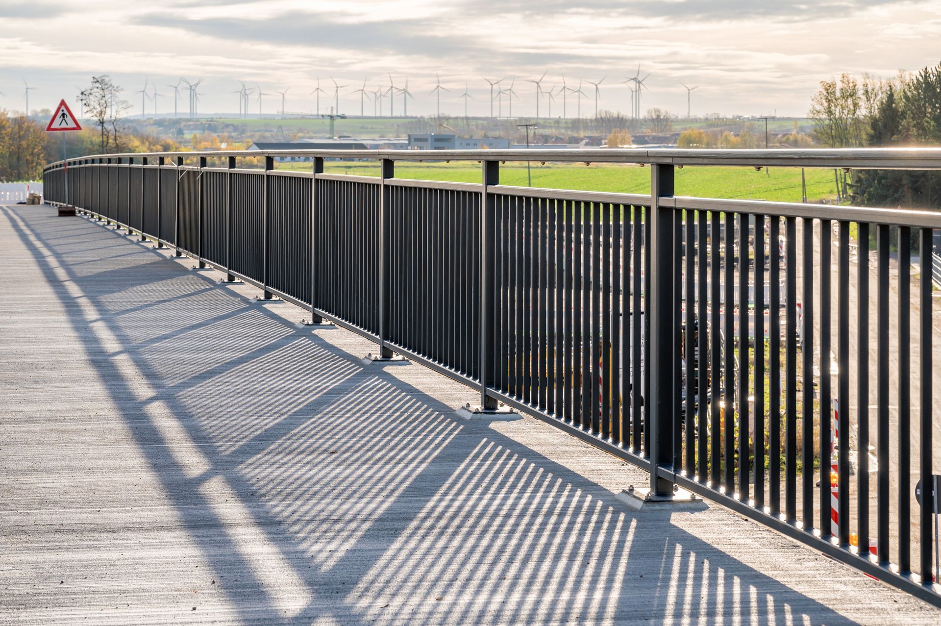 A bridge with a metal railing and shadows on the ground.
