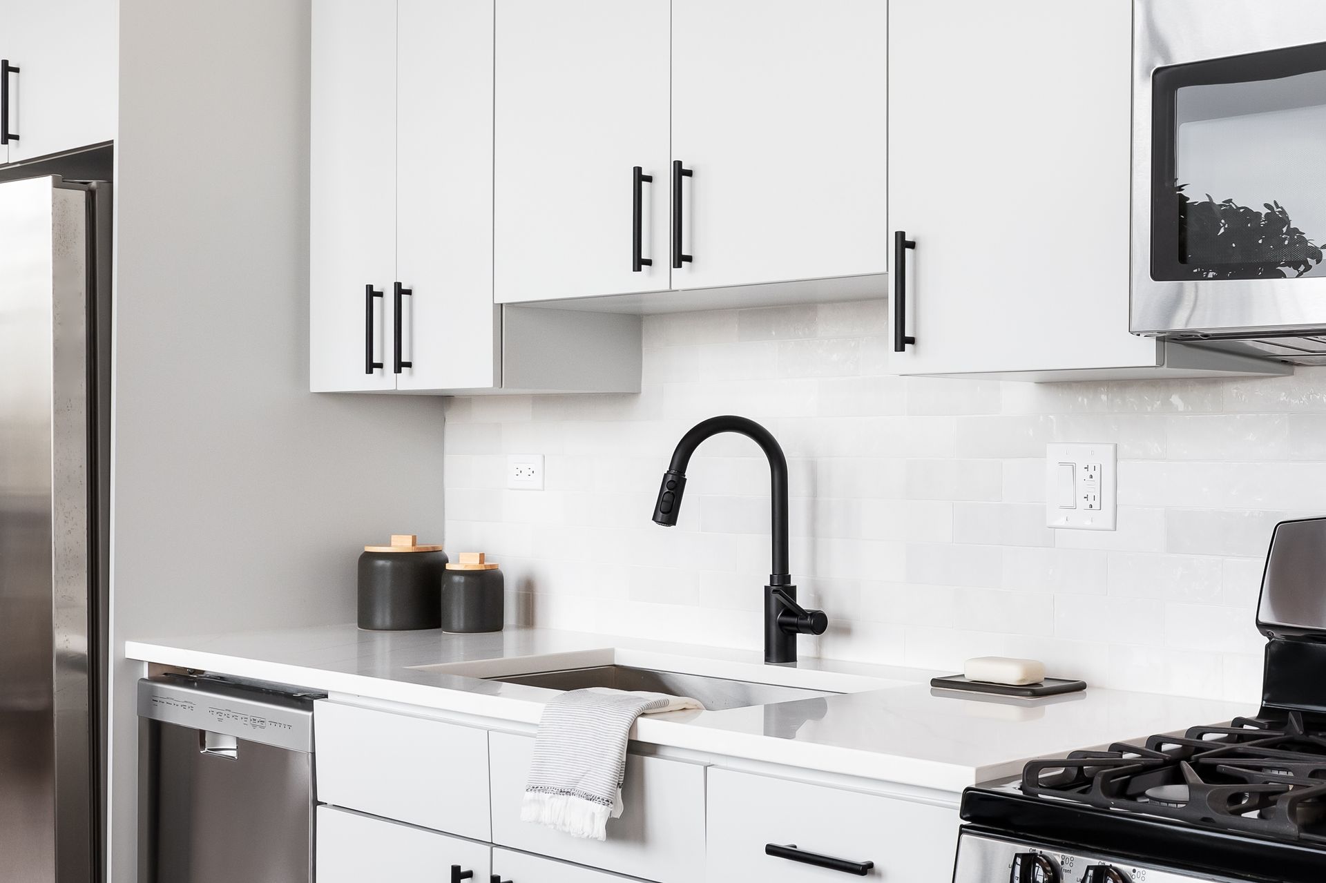 Cuisine blanche moderne avec électroménagers en acier inoxydable, robinetterie et quincaillerie noires, crédence en carreaux de métro blancs.