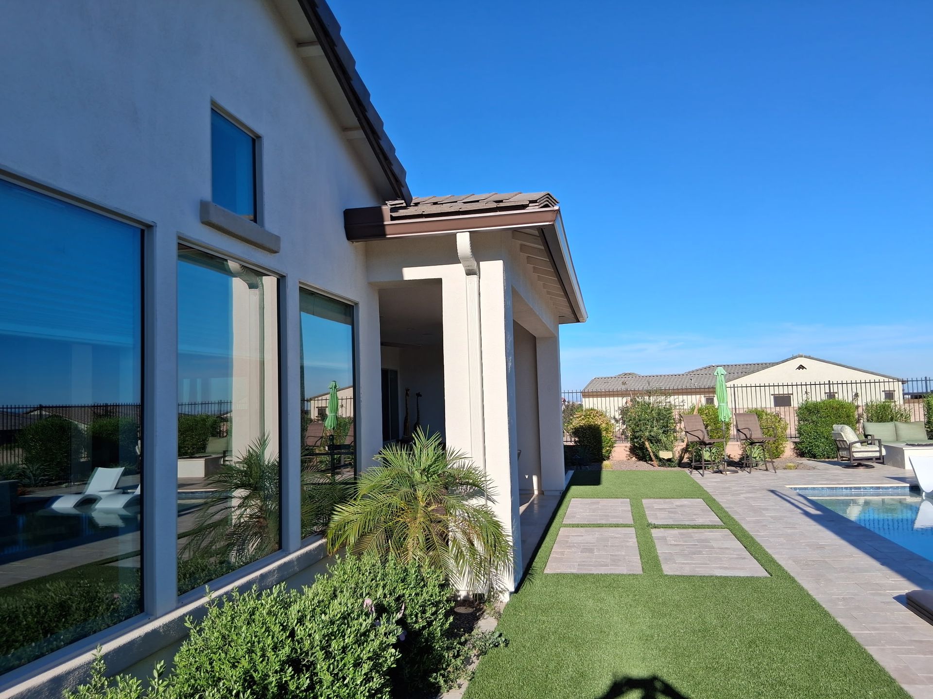 A light-colored house exterior with large windows and a covered patio overlooking a backyard pool on a sunny day.