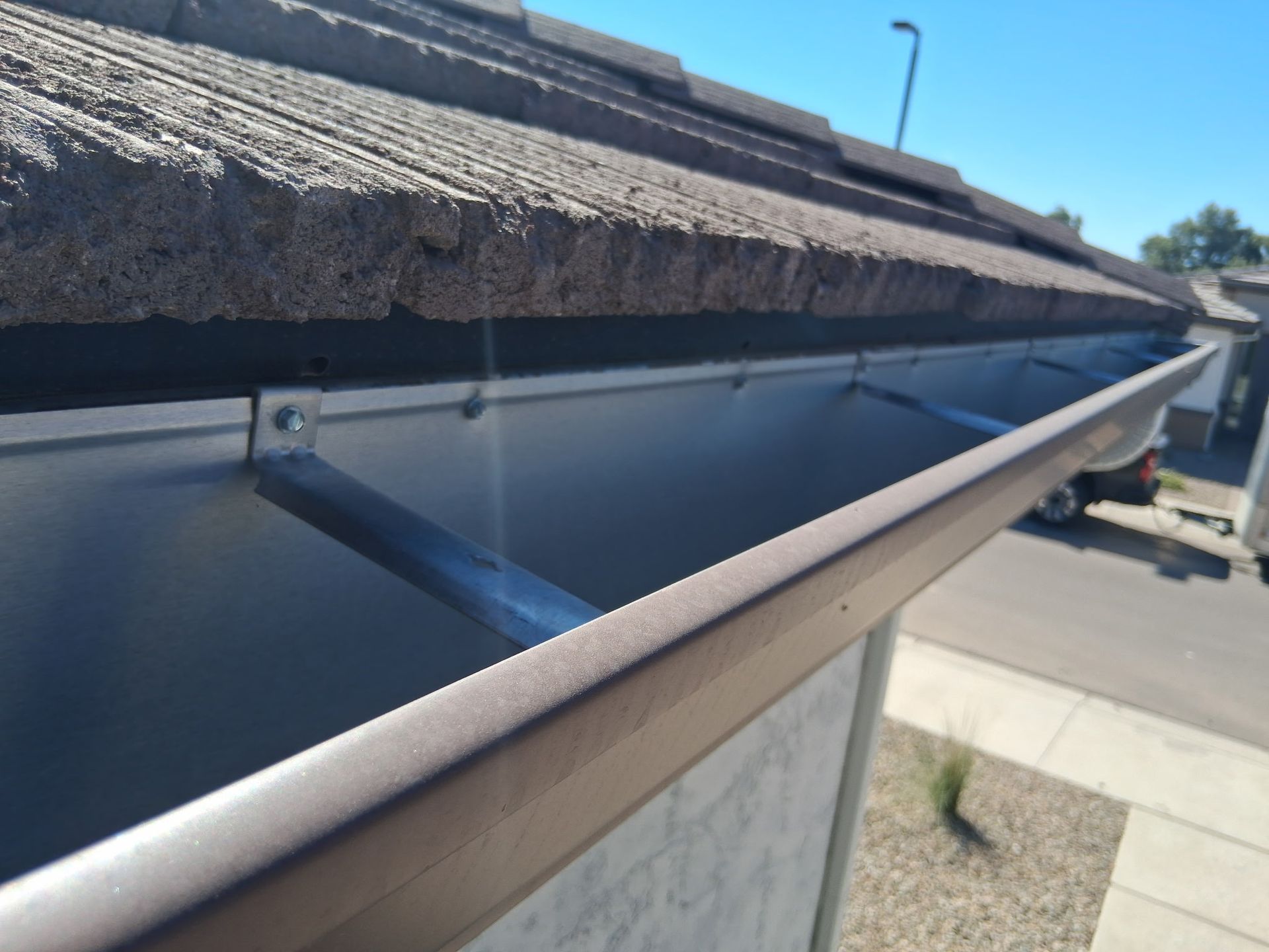 A close-up view of a metal gutter attached to the side of a tiled roof, showing the metal support brackets.