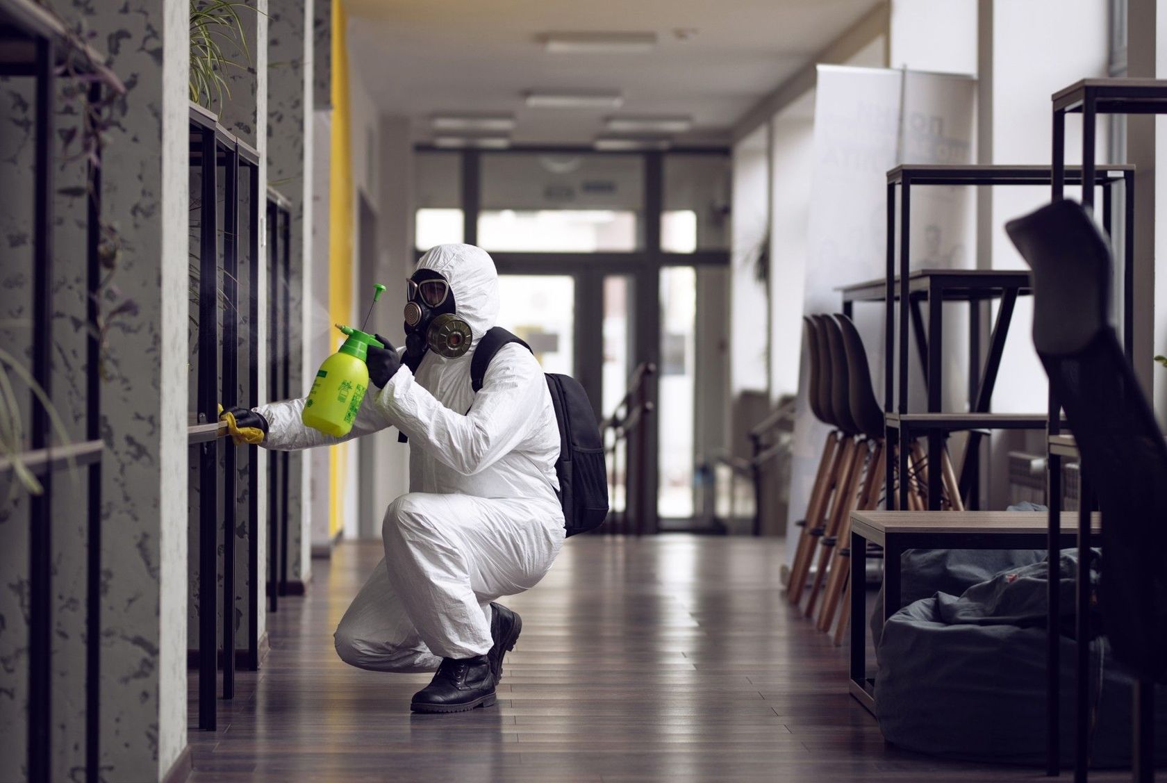 A man in a protective suit is spraying a room with a spray bottle.
